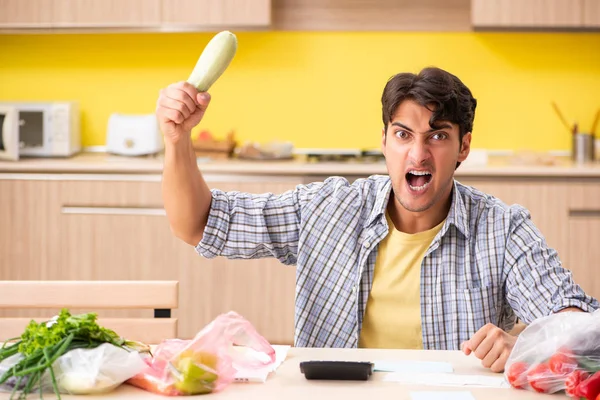 Joven calculando gastos para verduras en la cocina —  Fotos de Stock