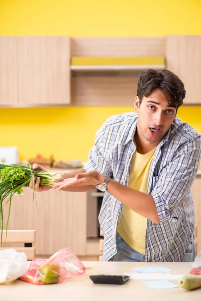 Joven calculando gastos para verduras en la cocina —  Fotos de Stock