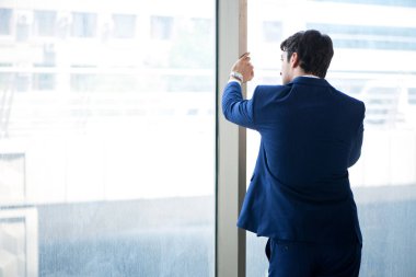 Genç yakışıklı işadamı pencerede duruyor. 