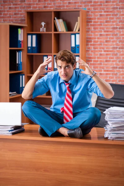 Jovem funcionário com excesso de trabalho sentado no escritório — Fotografia de Stock