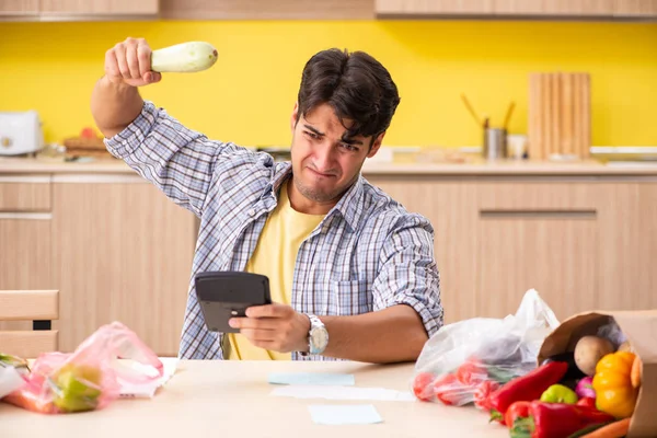 Joven calculando gastos para verduras en la cocina —  Fotos de Stock