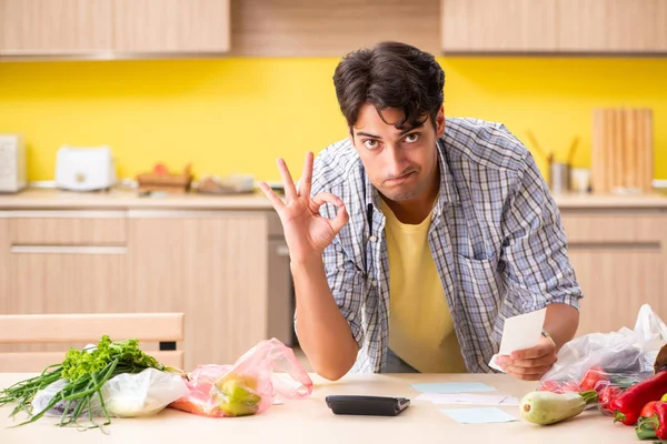Fiatalember kiszámítja a zöldségkiadásokat a konyhában — Stock Fotó