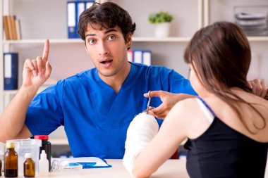 Kolu bandajlı genç kadın erkek doktor traumotologis 'i ziyaret ediyor.