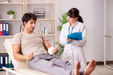 Kolu bandajlı genç adam kadın doktor travmatologunu ziyaret ediyor.