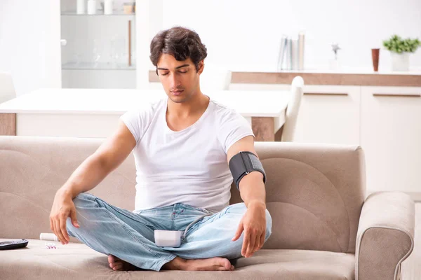 Homem jovem medindo a pressão arterial em casa — Fotografia de Stock