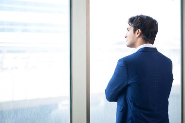 Genç yakışıklı işadamı pencerede duruyor. 