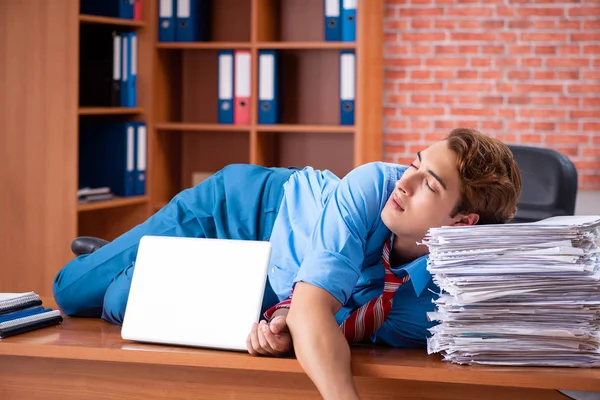 Jovem funcionário com excesso de trabalho sentado no escritório — Fotografia de Stock