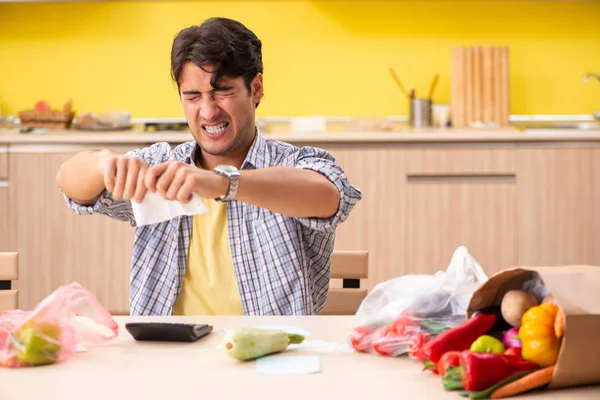 Joven calculando gastos para verduras en la cocina —  Fotos de Stock