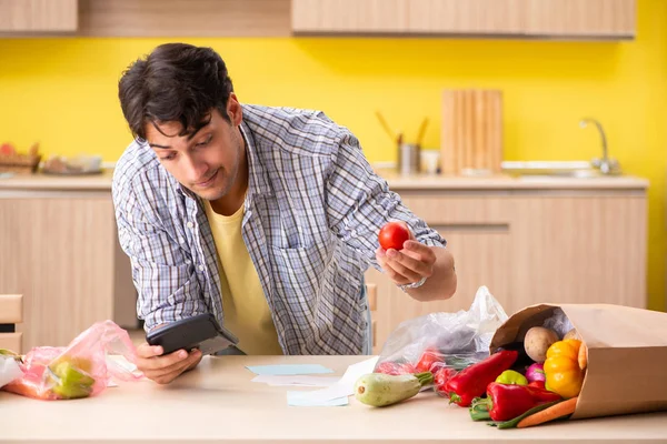 Joven calculando gastos para verduras en la cocina —  Fotos de Stock