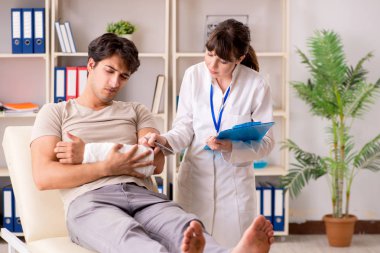 Kolu bandajlı genç adam kadın doktor travmatologunu ziyaret ediyor.