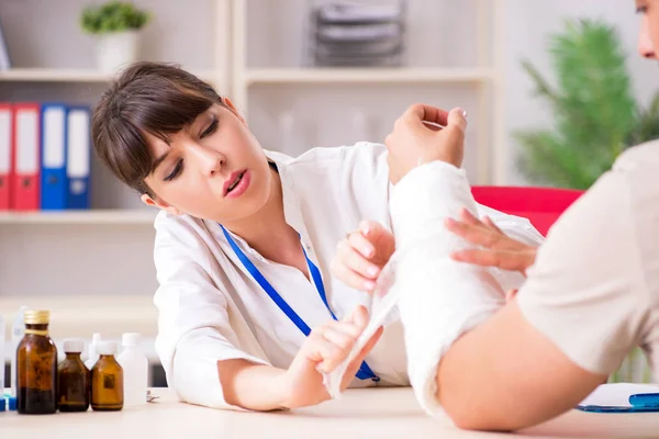 Giovane uomo con il braccio fasciato in visita medico traumatologo femminile — Foto Stock