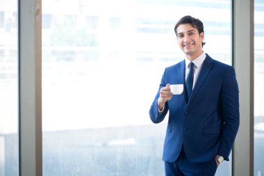 Genç yakışıklı işadamı pencerede duruyor. 