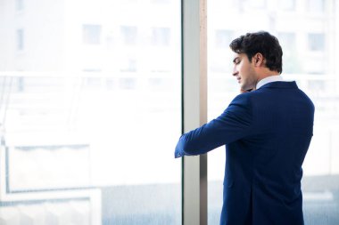 Genç yakışıklı işadamı pencerede duruyor. 