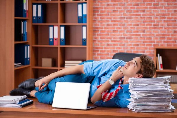 Jovem funcionário com excesso de trabalho sentado no escritório — Fotografia de Stock