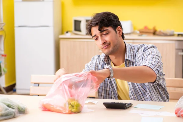 Joven calculando gastos para verduras en la cocina —  Fotos de Stock