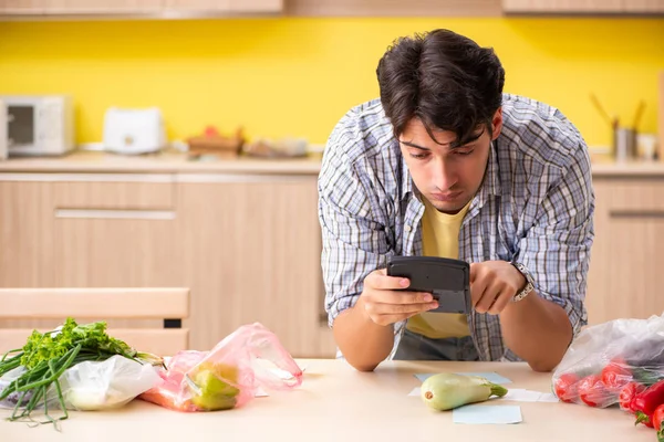 Joven calculando gastos para verduras en la cocina —  Fotos de Stock