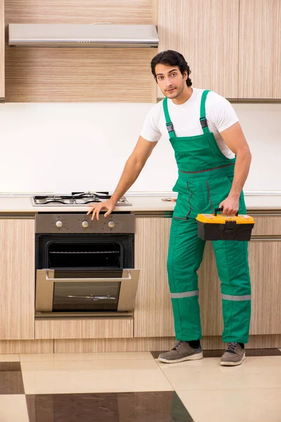 Jovem empreiteiro reparação forno na cozinha — Fotografia de Stock