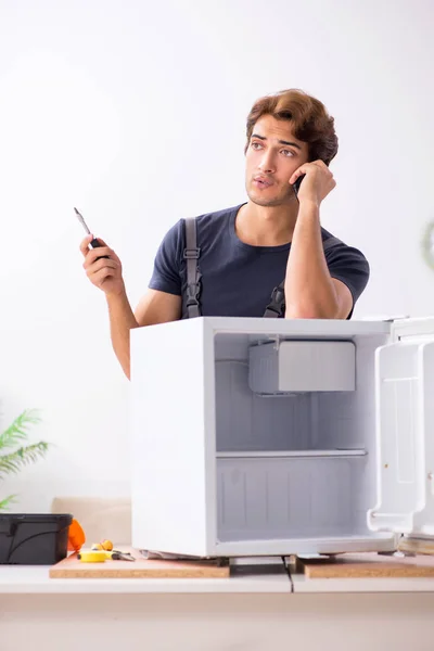 Young handsome contractor repairing fridge