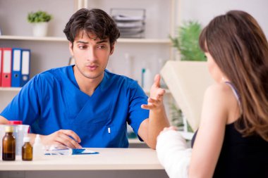 Kolu bandajlı genç kadın erkek doktor traumotologis 'i ziyaret ediyor.