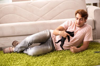 Genç adam evde kedi yavrusuyla oynuyor.