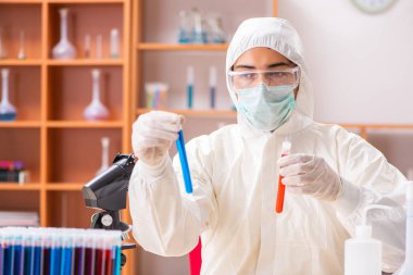 Laboratuvarda çalışan koruyucu elbise giyen genç bir biyokimyacı.