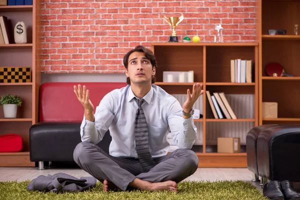 Young handsome employee doing yoga in the office