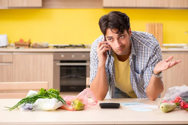 Joven calculando gastos para verduras en la cocina —  Fotos de Stock