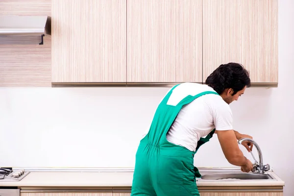 Молодой сантехник ремонтирует кран на кухне — стоковое фото