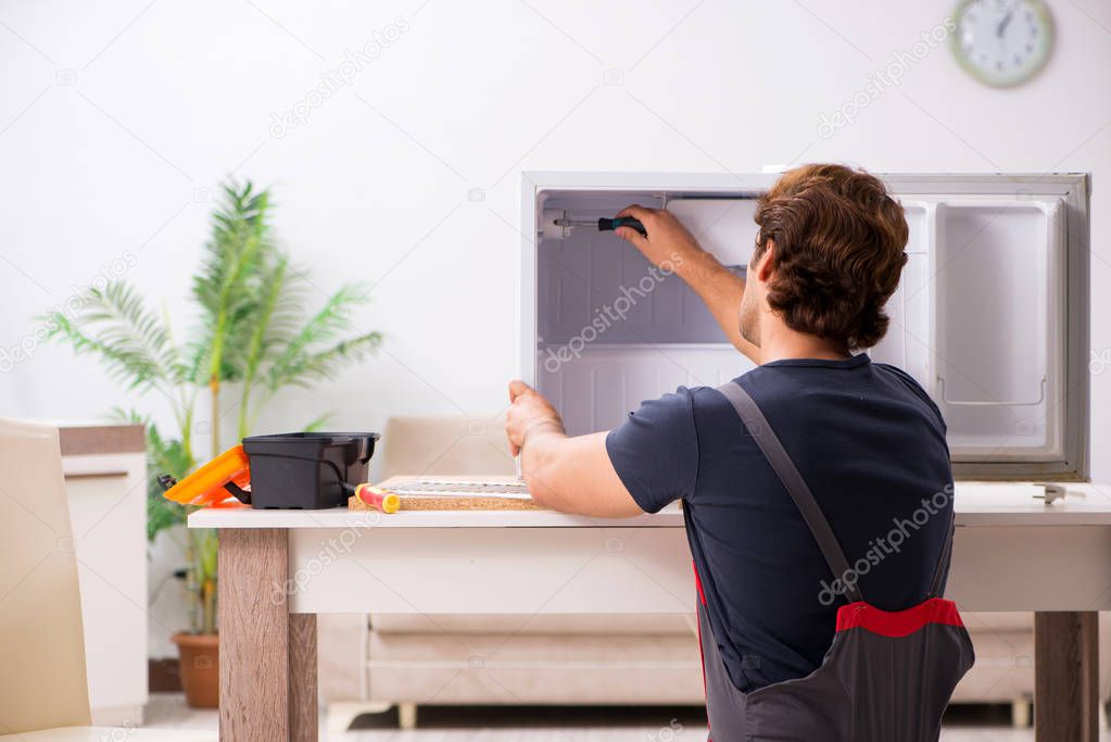 Young handsome contractor repairing fridge 