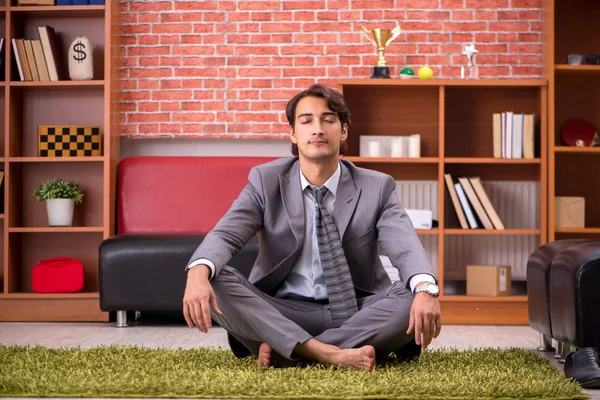 Young handsome employee doing yoga in the office