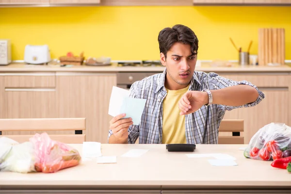 Joven calculando gastos para verduras en la cocina —  Fotos de Stock