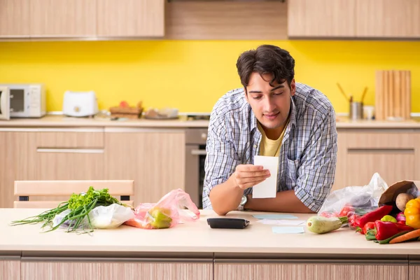 Joven calculando gastos para verduras en la cocina —  Fotos de Stock