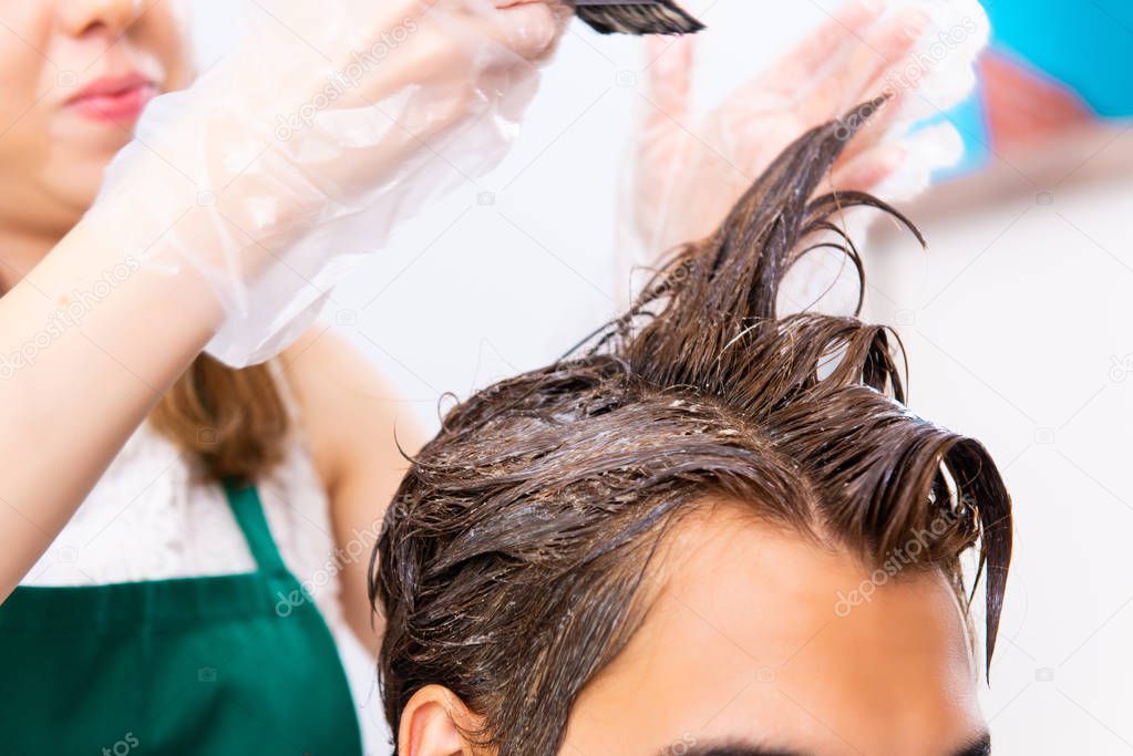 Woman hairdresser applying dye to man hair