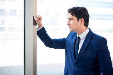 Genç yakışıklı işadamı pencerede duruyor.