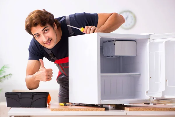 Young handsome contractor repairing fridge