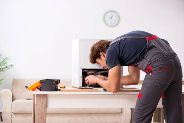 Young handsome contractor repairing fridge