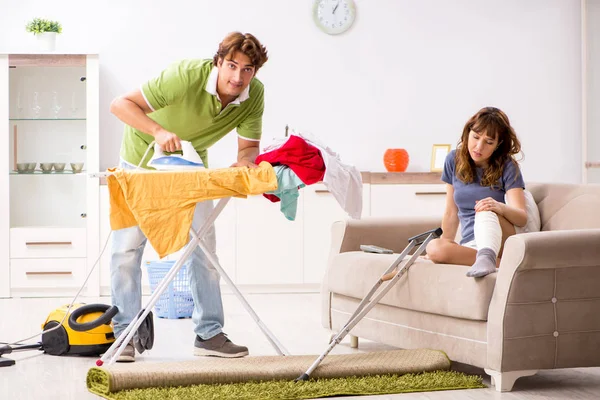 Husband helping leg injured wife in housework — Stock Photo, Image