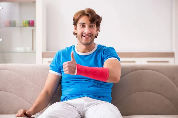 Jeune homme avec un bras blessé assis sur le canapé — Photo