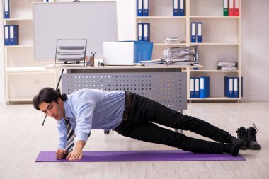 Genç yakışıklı erkek çalışanımız ofiste egzersiz yapıyor.