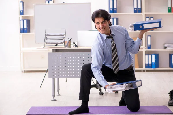 Young handsome male employee doing exercises in the office — Stock Photo, Image