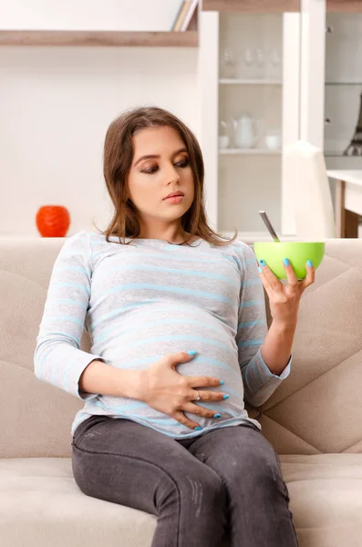 Mujer embarazada joven sentada en el sofá en casa — Foto de Stock