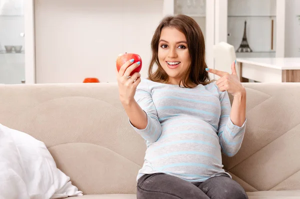 Młoda kobieta w ciąży, siedząc na kanapie w domu — Zdjęcie stockowe