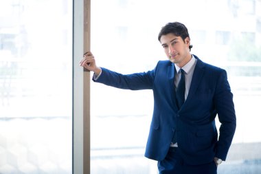 Genç yakışıklı işadamı pencerede duruyor. 