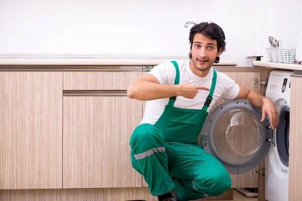 Молодой подрядчик ремонтирует стиральную машину на кухне — стоковое фото