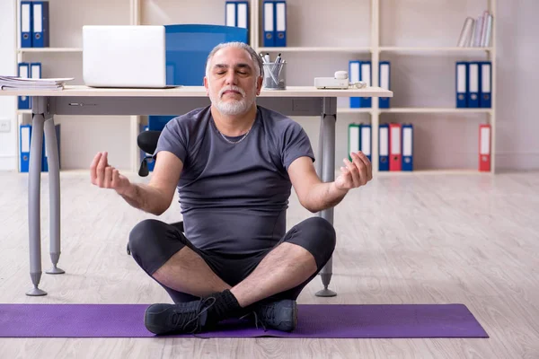 White bearded old man employee doing exercises in the office