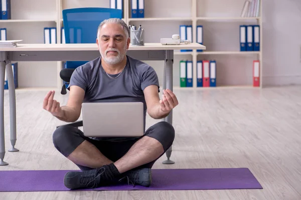 White bearded old man employee doing exercises in the office — Stock Photo, Image