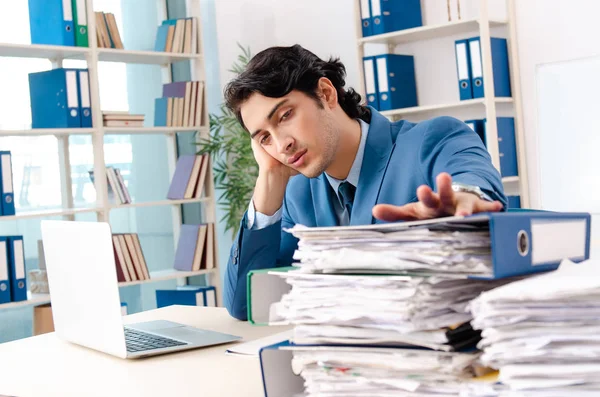 Joven empleado varón guapo con demasiado trabajo en la oficina — Foto de Stock