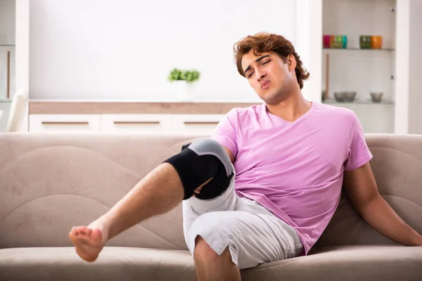 Młody człowiek z poszkodowanej kolana odzyskiwanie w domu — Zdjęcie stockowe