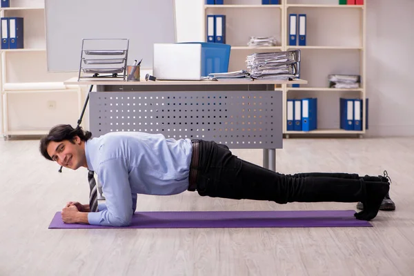 Young handsome male employee doing exercises in the office