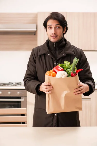 Ung vacker man med grönsaker i köket — Stockfoto